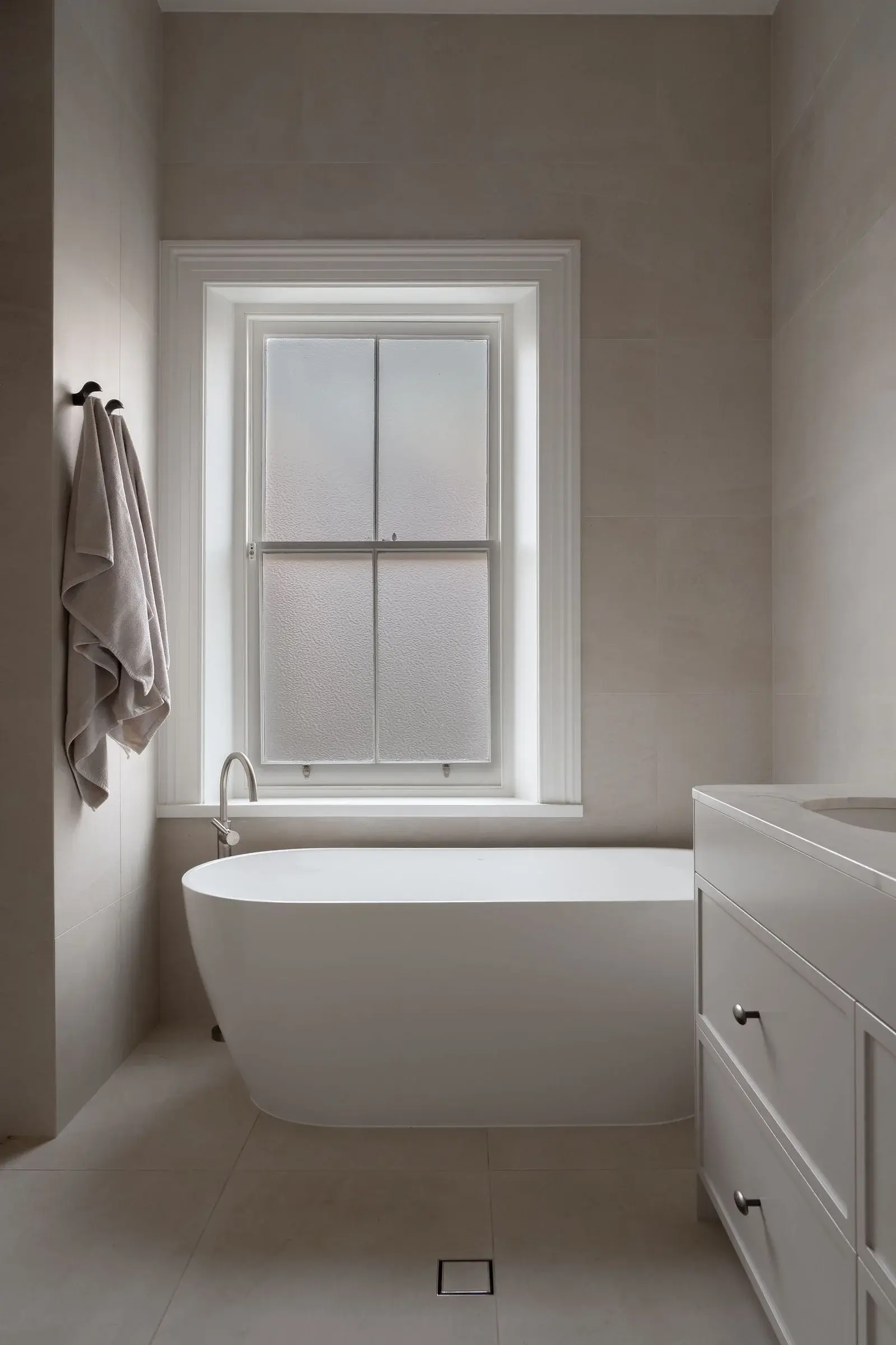 Freestanding bath beneath a frosted heritage window